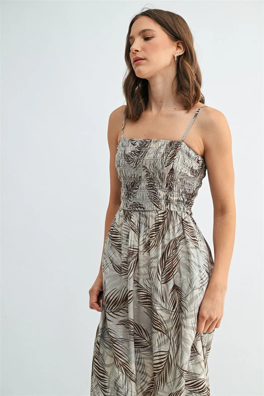A flowing sleeveless leaf print smocking midi dress with square neckline and gray brown tropical leaf design