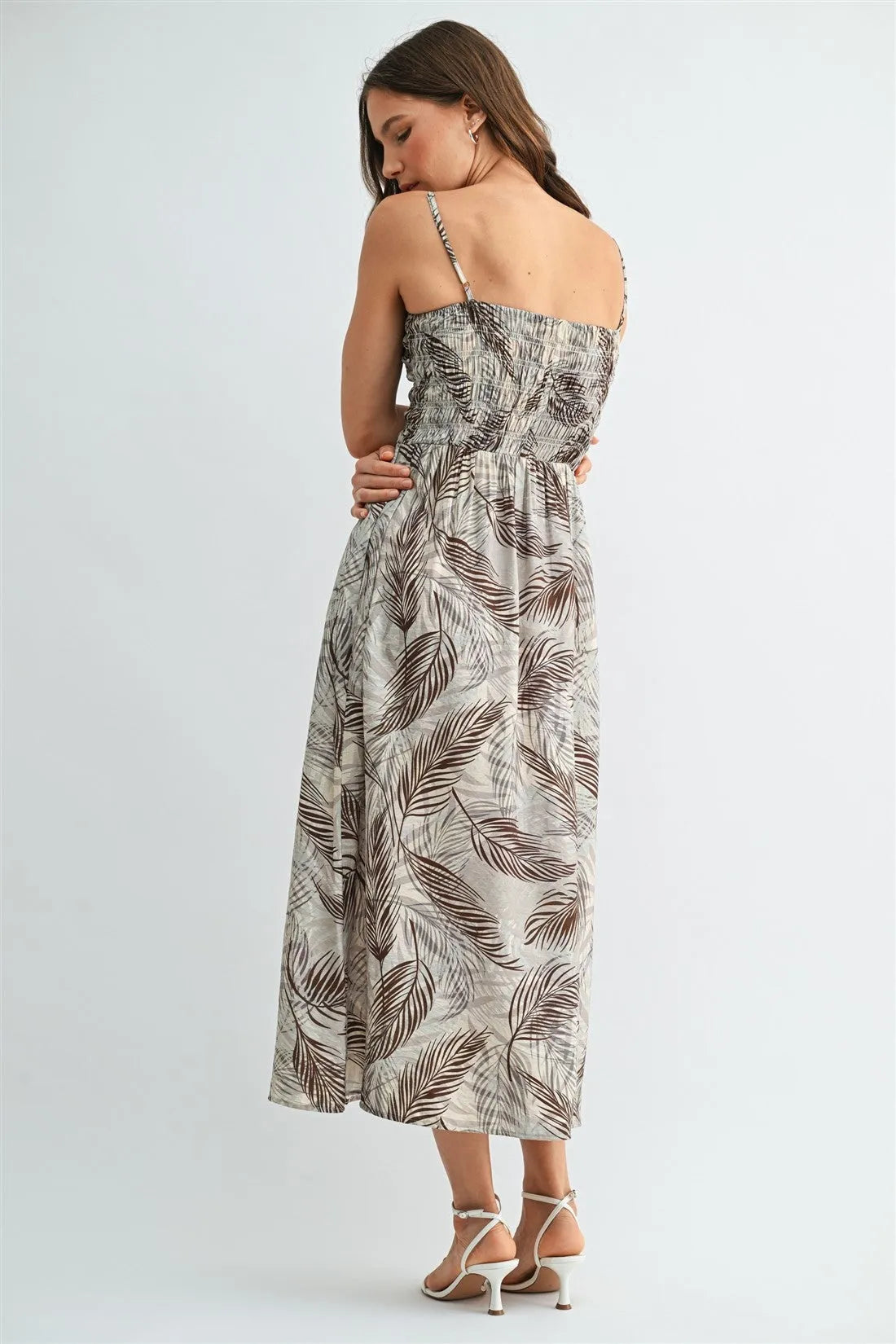 A flowing sleeveless leaf print smocking midi dress in brown and beige tropical leaf patterns on a light background