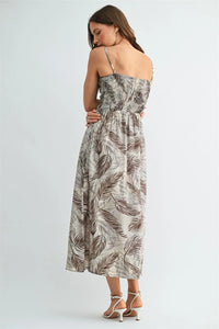 A flowing sleeveless leaf print smocking midi dress in brown and beige tropical leaf patterns on a light background