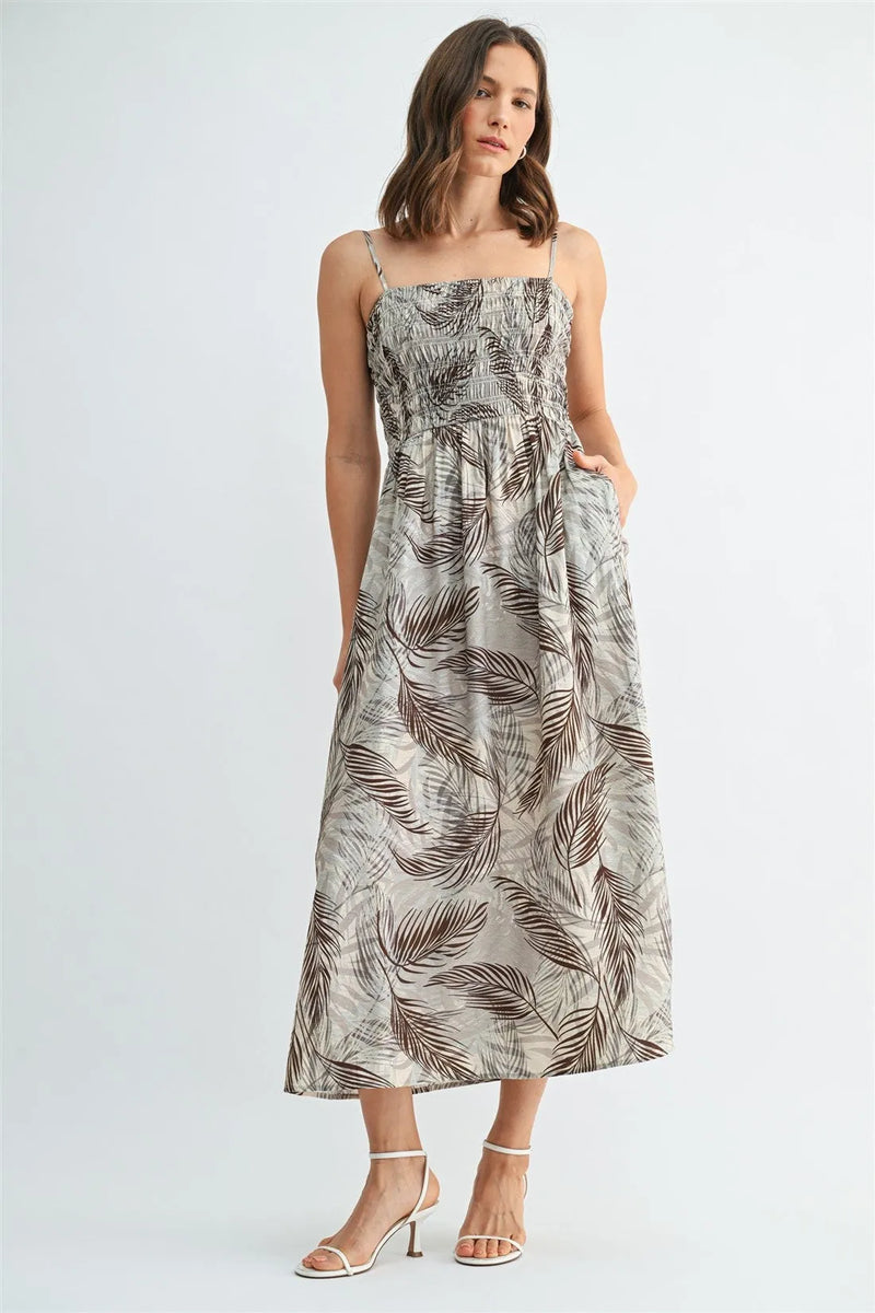 A flowing beige leaf print smocking midi dress with delicate spaghetti straps and an elegant brown leaf pattern