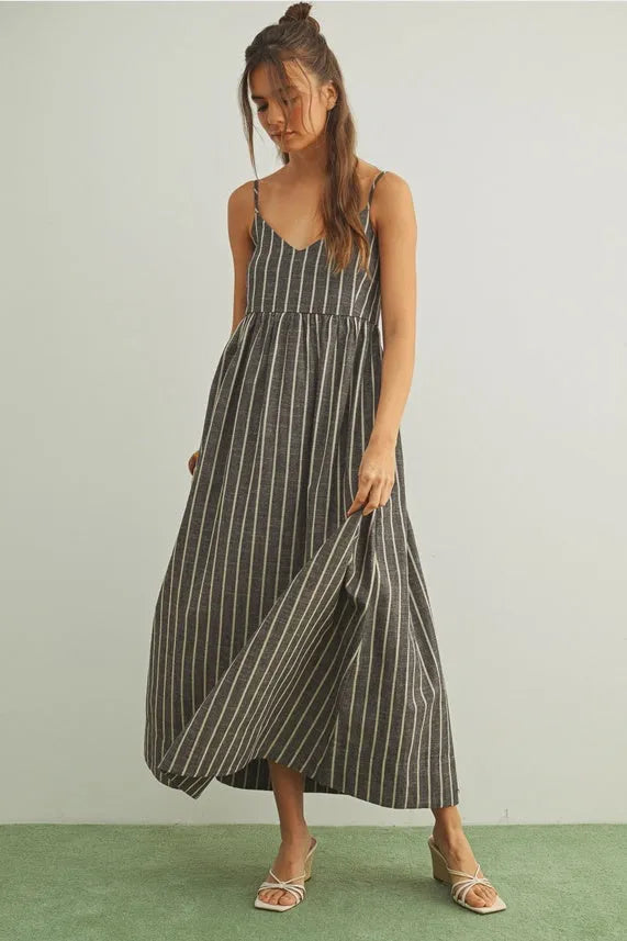 A flowing sleeveless midi dress with dark gray and white vertical stripe pattern and thin spaghetti straps featuring stripe pattern smocked back