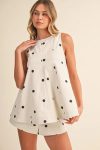 A sleeveless off-white top with black polka dots and flared hem paired with polka dot denim elastic short