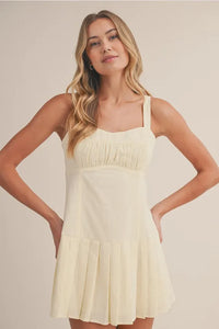 A soft cream-colored shirring bra cotton mini dress with a square neckline, gathered bodice, and pleated skirt