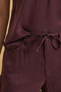 A soft deep burgundy satin jumpsuit featuring a tied waistband and subtle side pockets with loose fit wide legs