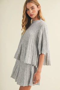 A soft light gray rib knit two-piece set with a wide rib knit cape-style top and matching pleated skirt