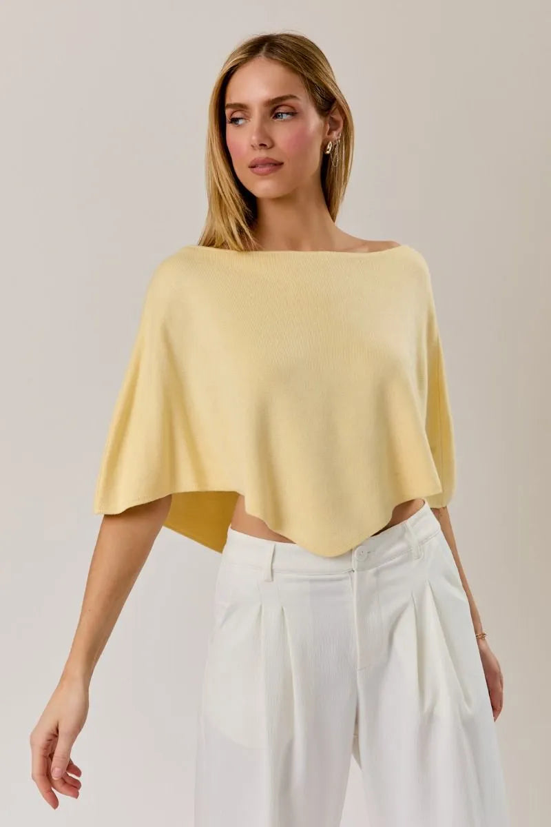 A soft pale yellow off-the-shoulder poncho knit top with a relaxed slouchy neck line poncho silhouette