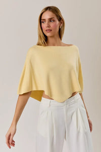 A soft pale yellow off-the-shoulder poncho knit top with a relaxed slouchy neck line poncho silhouette