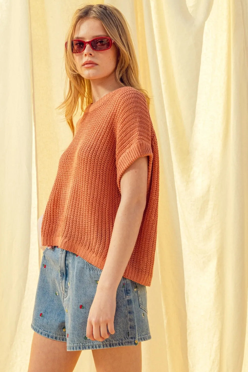 A soft rust-orange dolman sleeve knitted top with ribbed texture and short sleeves made from cozy yarn