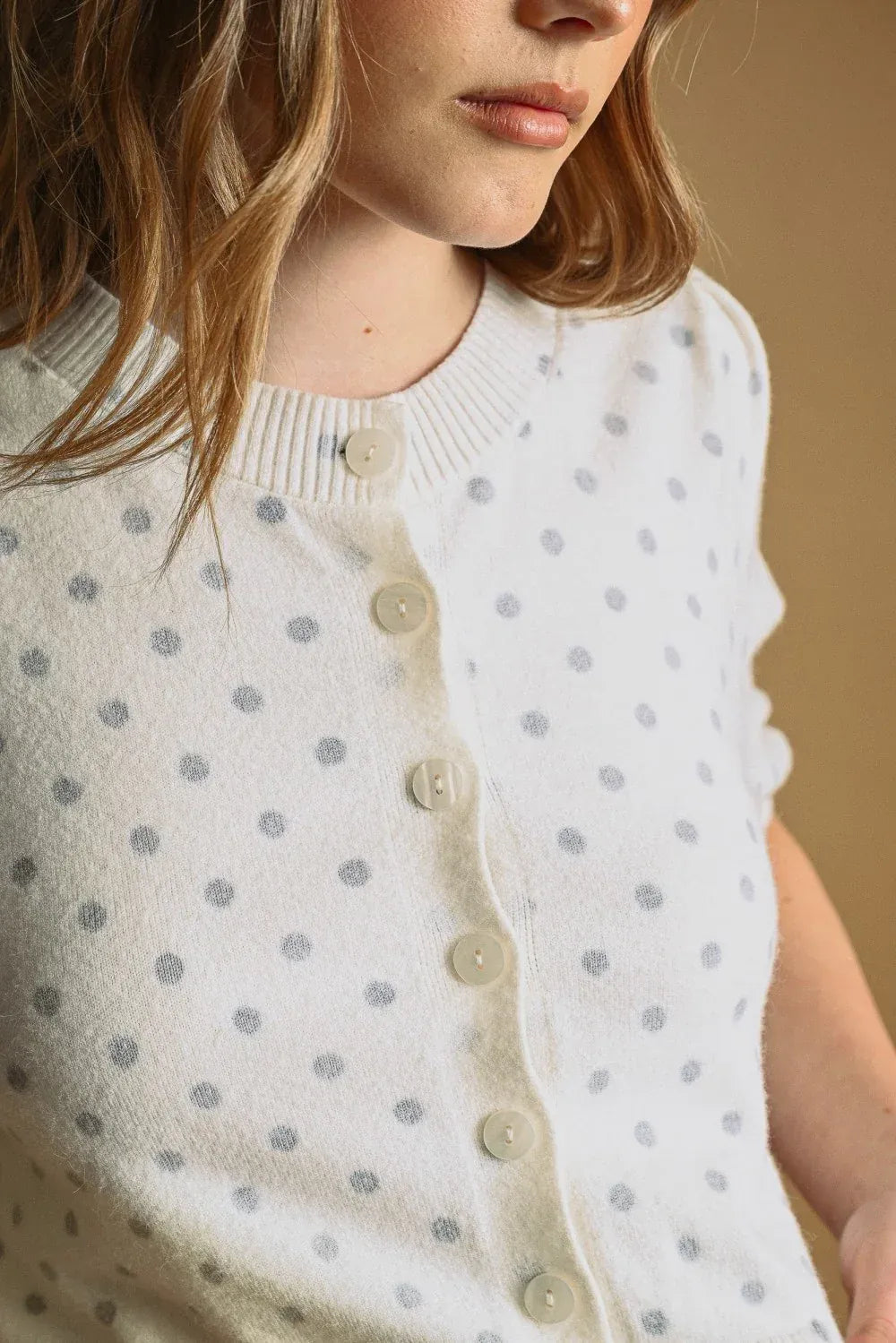 A soft white knit polka dot short sleeve cardigan with subtle gray dots and cream-colored buttons
