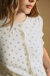 A soft white knit polka dot short sleeve cardigan with subtle gray dots and cream-colored buttons