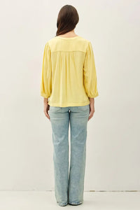 A soft yellow long-sleeved blouse with a gathered bodice and puffed notched y-neck volume sleeves