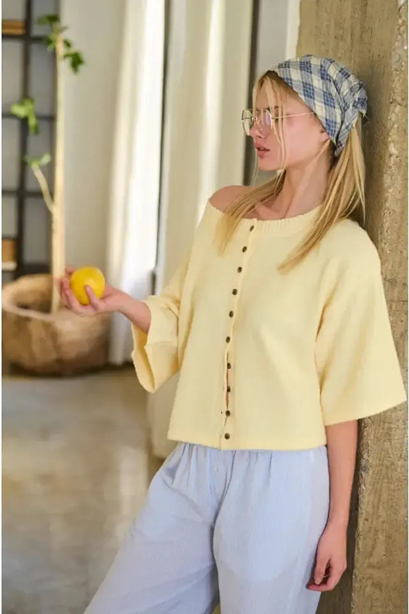 A soft yellow off-the-shoulder wide sleeve button knit fabric cardigan with black buttons