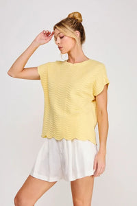 A soft yellow scallop pattern relaxed knit top with short sleeves textured with a wavy pattern and scalloped hem