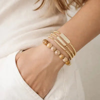 Gold beaded stretch bracelet with gold-toned links smooth brown beads and a rectangular charm in a stack