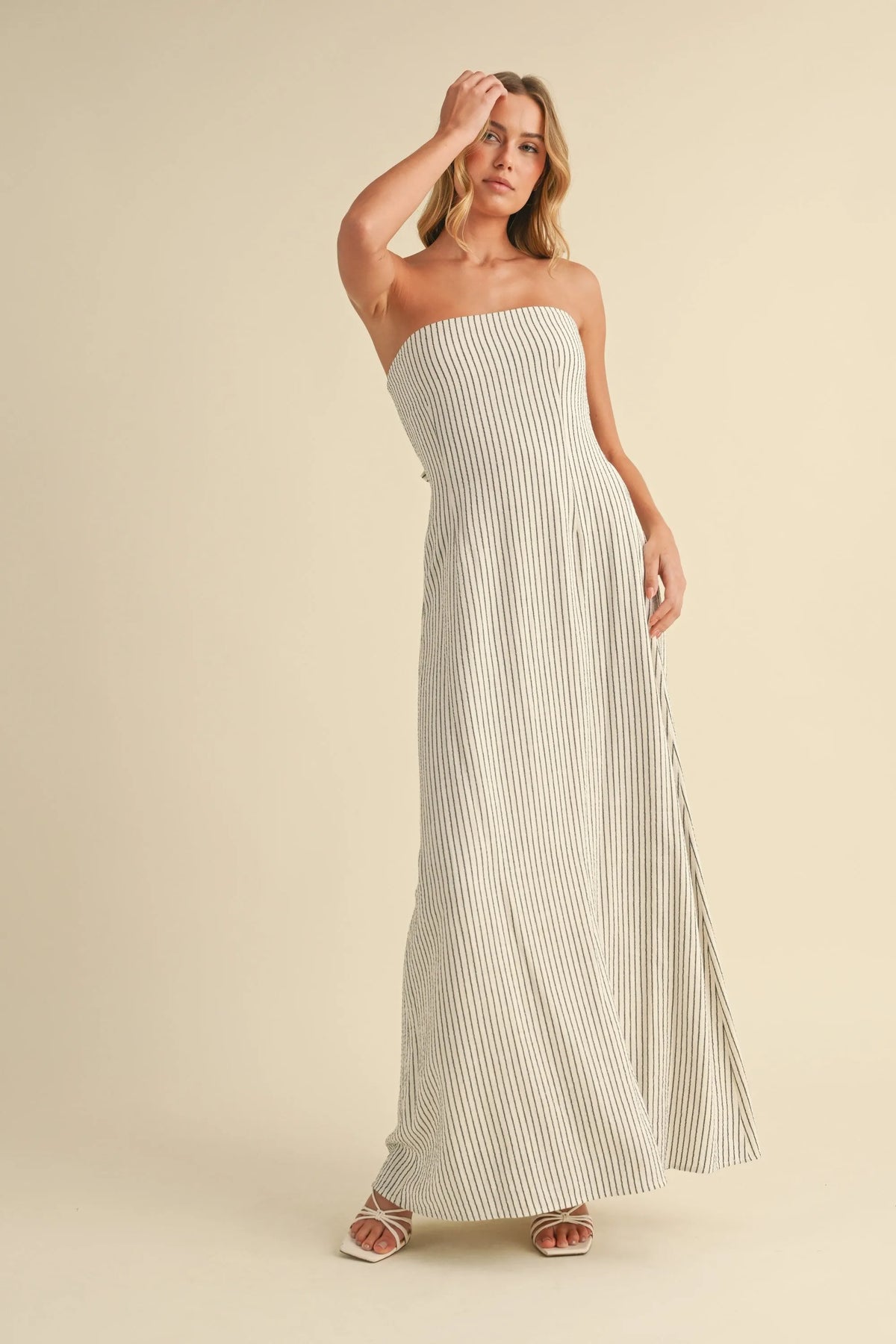 A flowing off-white strapless maxi dress with thin navy blue vertical stripes and a long back tie strapless maxi design