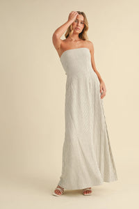 A flowing off-white strapless maxi dress with thin navy blue vertical stripes and a long back tie strapless maxi design