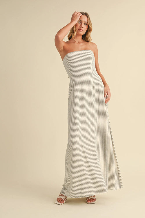 A flowing off-white strapless maxi dress with thin navy blue vertical stripes and a long back tie strapless maxi design
