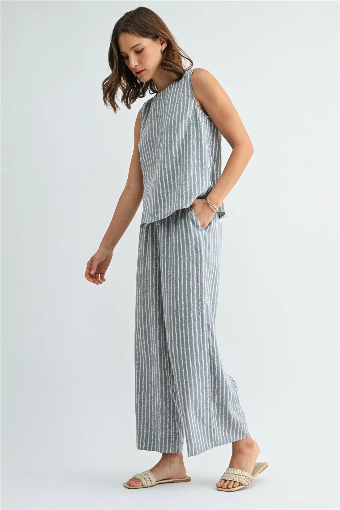 A woman wears soft gray stripe straight leg elastic pants with thin white vertical stripes and a matching sleeveless top