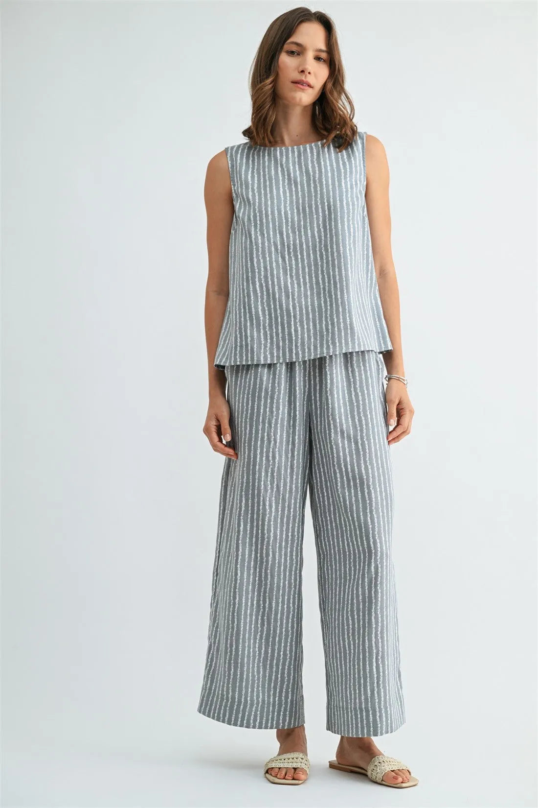 A woman wearing light blue and white striped straight leg elastic pants made of linen with a matching sleeveless top