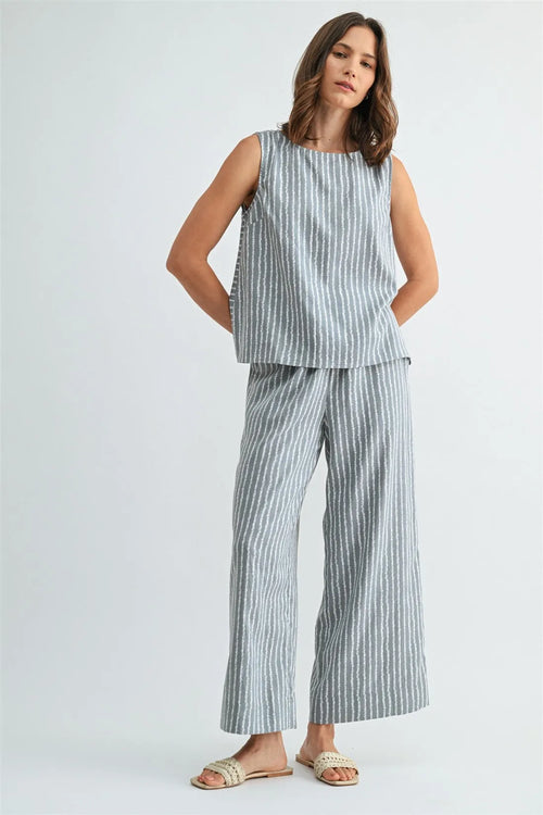 A woman wearing light blue and white vertical stripe straight leg elastic linen blend pants with a sleeveless top
