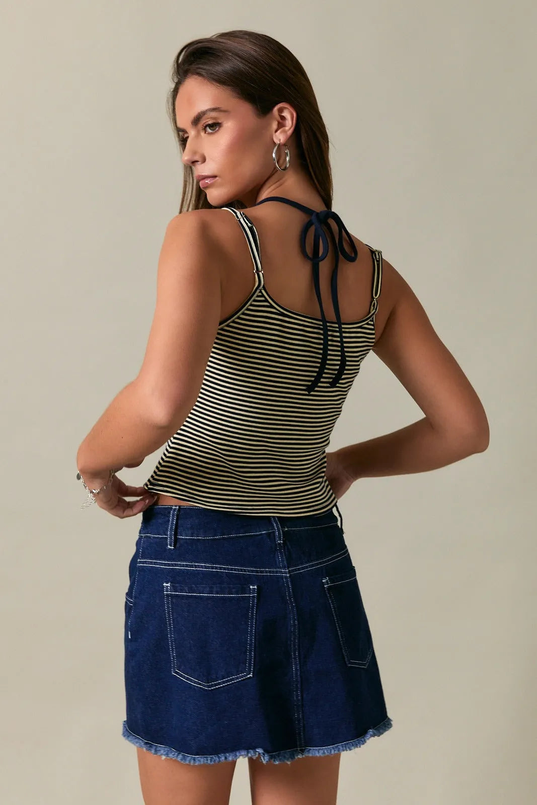 Back view of a striped black and beige two tone halter neckline tank top with thin straps tied into bows