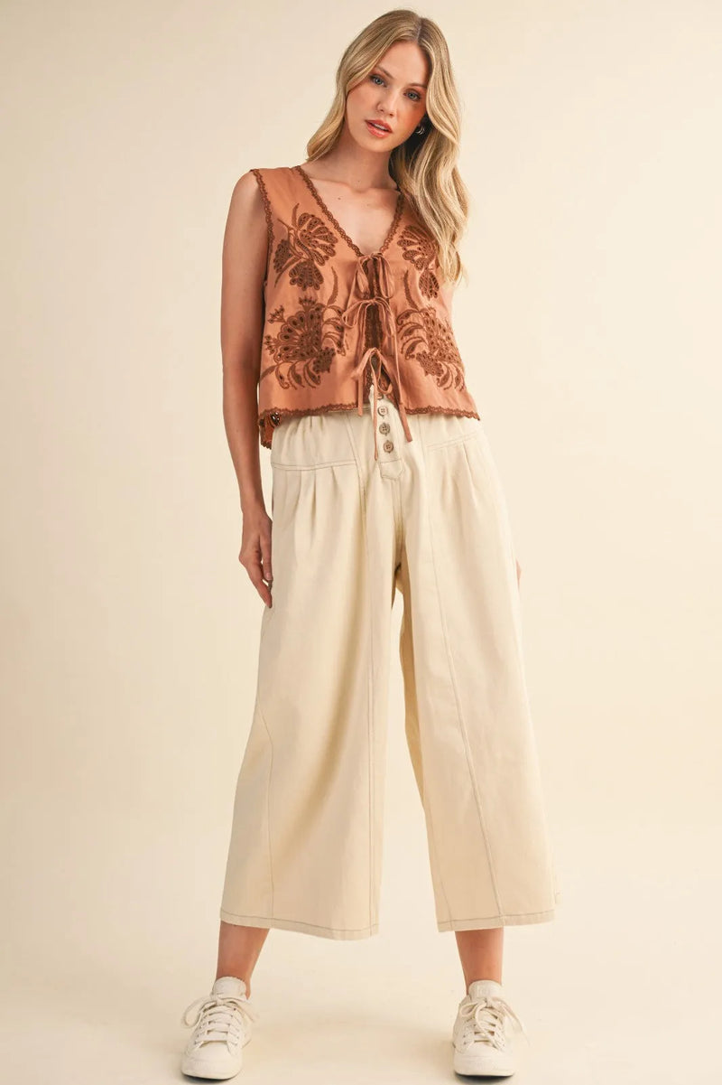 A tan sleeveless top with floral pattern and lace trim paired with high rise super wide leg crop denim jeans