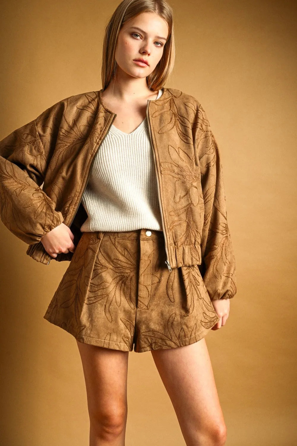 Tan suede bomber jacket with embroidered leaf pattern complementing suede floral textured shorts collection
