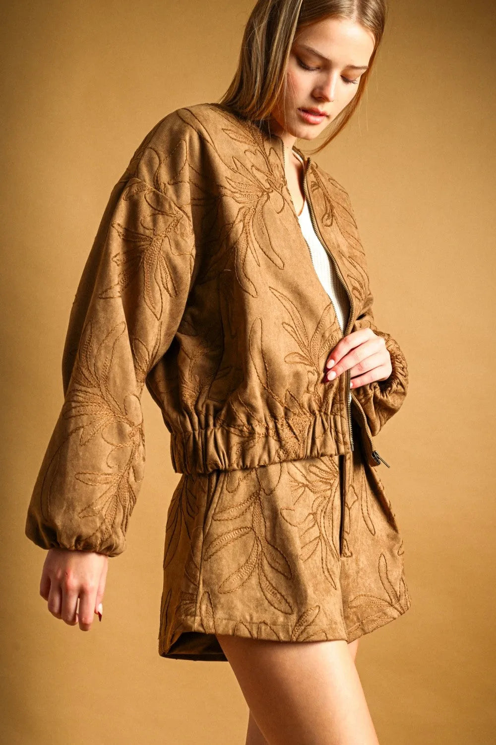 Tan suede bomber jacket with intricate leaf embroidery and elasticated waistband complements suede floral textured shorts
