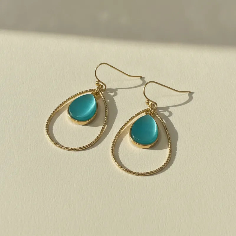 Elegant gold teardrop hoop earrings featuring teal cats eye stone cabochons and gold-toned wireframe design
