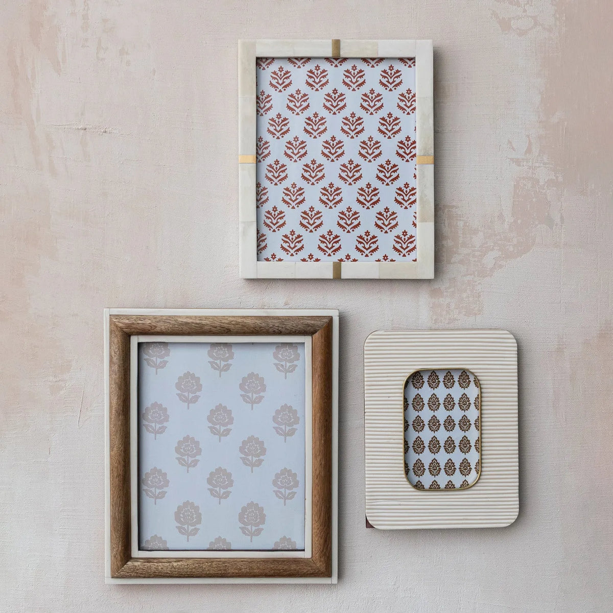Three distinct photo frames including a cream resin ribbed photo frame with brass inlay displayed against a textured wall