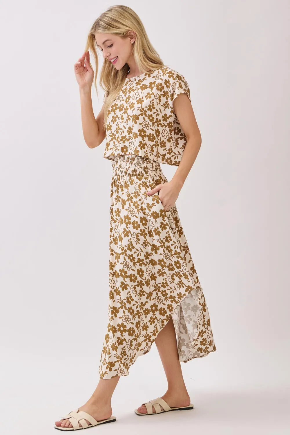 A flowing two-piece floral dress in soft beige with a smocked waistband midi skirt and relaxed fit top featuring brown blossoms