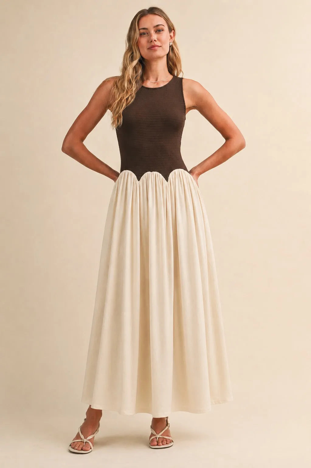 A sleeveless knit crinkle maxi dress with a dark brown fitted bodice and off-white pleated skirt in flowing fabric