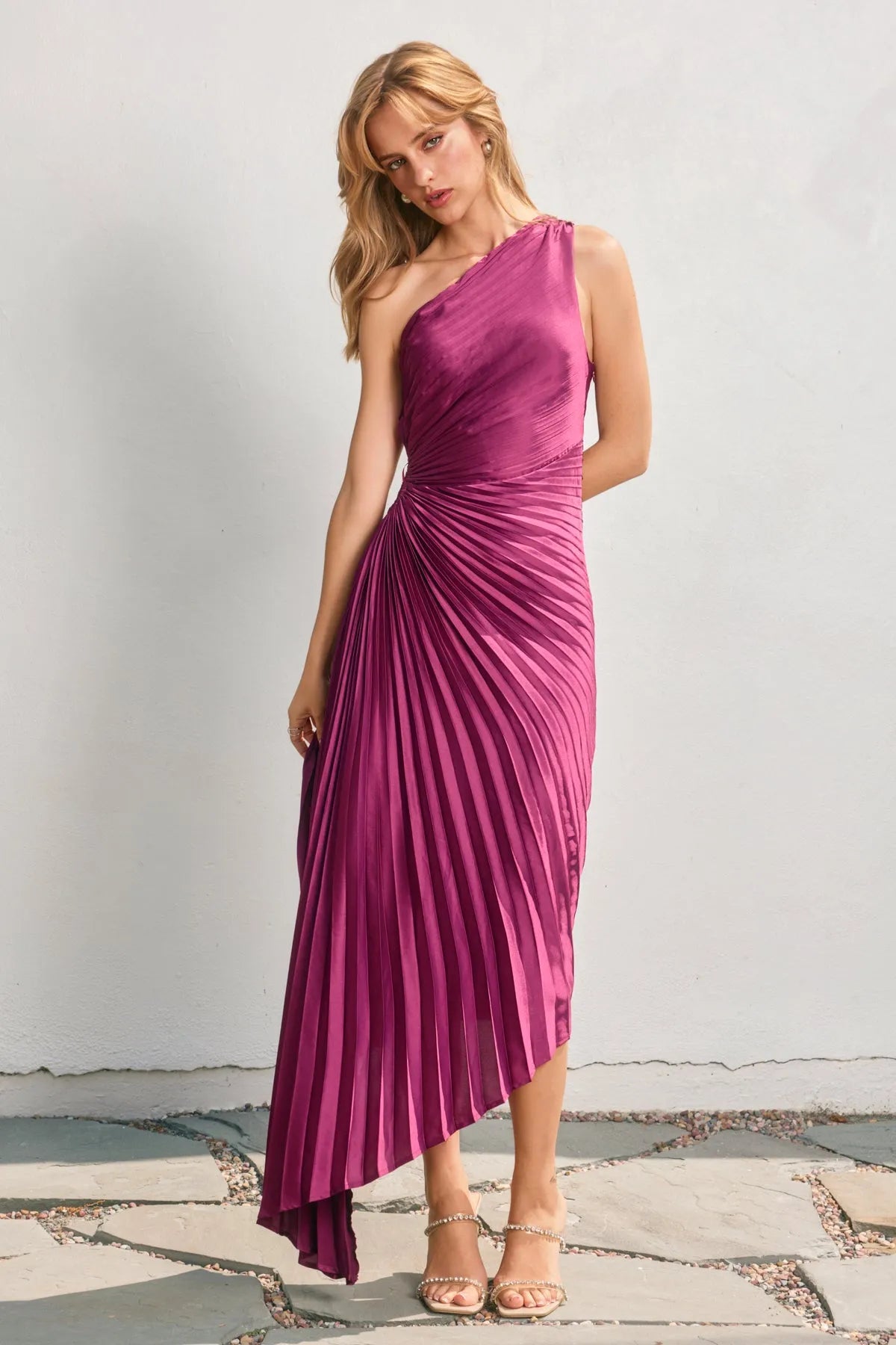 A vibrant magenta satin one shoulder asymmetrical pleated dress with a midi pleated skirt in luxury fabric