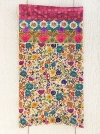 A vibrant boho bandeau headband with cream borders featuring multi-colored floral patterns and a bold pink top border