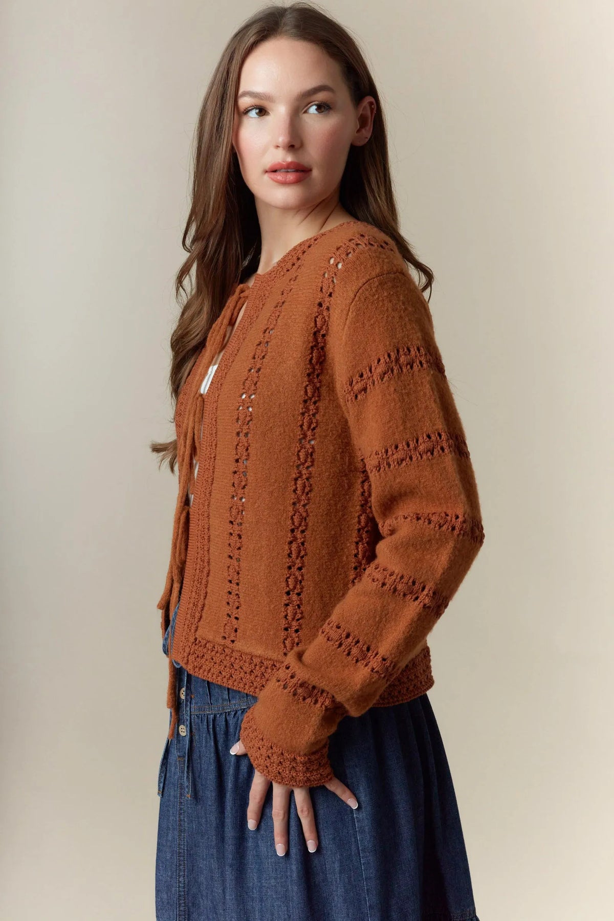 A warm terracotta knitted cardigan with hole stripe bows detailing and a front tie closure in long sleeves