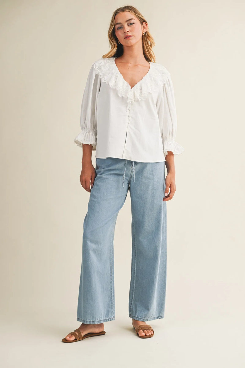 White blouse with ruffled neckline and puffed sleeves paired with relaxed denim pants with drawstring waist