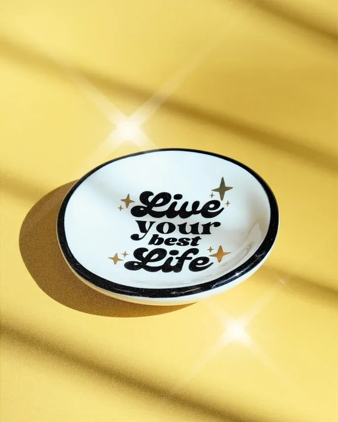 White ceramic ring dish with black rim and live your best life text accented by gold stars perfect for women’s boho chic clothing fans