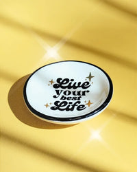White ceramic ring dish with black rim and live your best life text accented by gold stars perfect for women’s boho chic clothing fans