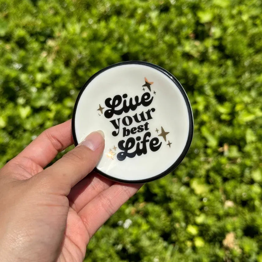 White ceramic ring dish with black rim and live your best life text accented by gold stars for women’s boho chic clothing fans