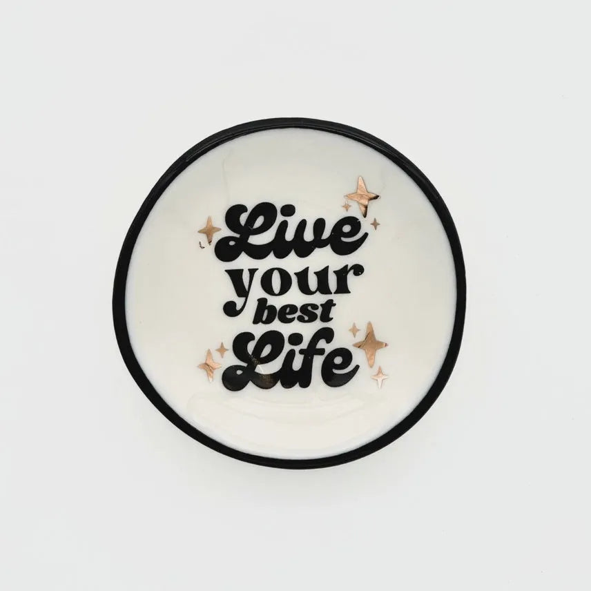 White ceramic ring dish with black rim featuring live your best life text and rose gold star accents for women’s boho chic clothing fans