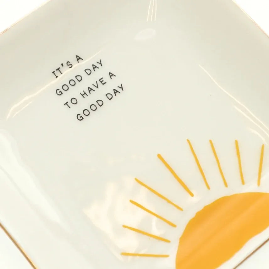 White ceramic trinket tray with gold rim featuring a yellow sun design and the phrase it is a good day to have a good day