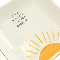 White ceramic trinket tray with gold rim featuring a yellow sun design and the phrase it is a good day to have a good day
