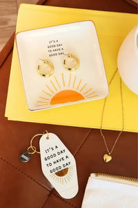 White ceramic trinket tray with gold rim sunburst design and phrase its a good day to have a good day printed in black