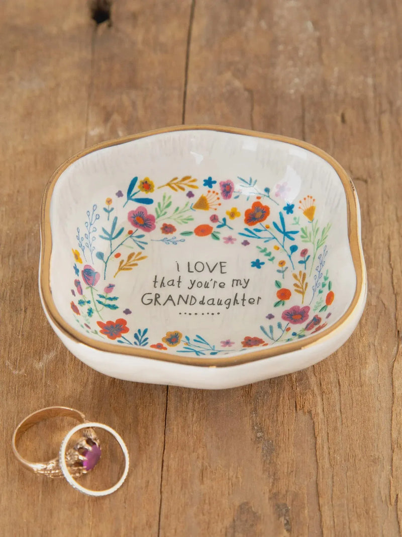A white ceramic antiqued trinket bowl with a gold rim, colorful floral patterns, and granddaughter inscription