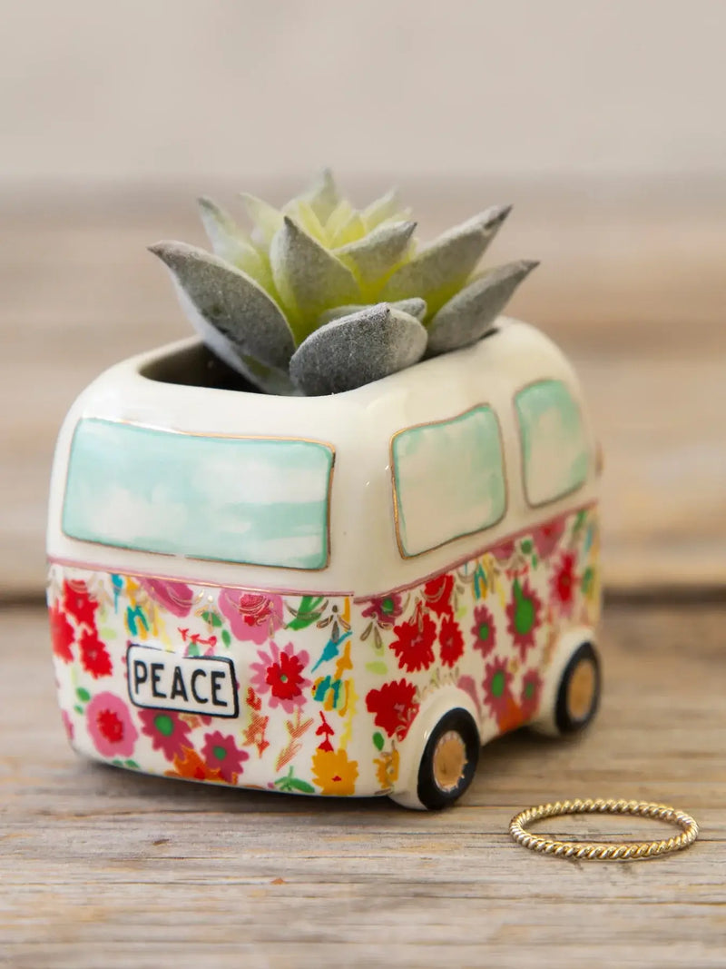 A white ceramic van-shaped planter with vibrant floral design and peace text holding a soft gray tiny faux succulent