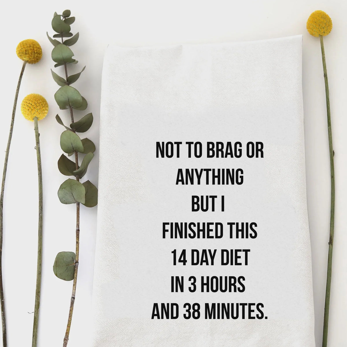 White cotton 14 day diet tea towel with black text humorously stating completion time of the 14 day diet