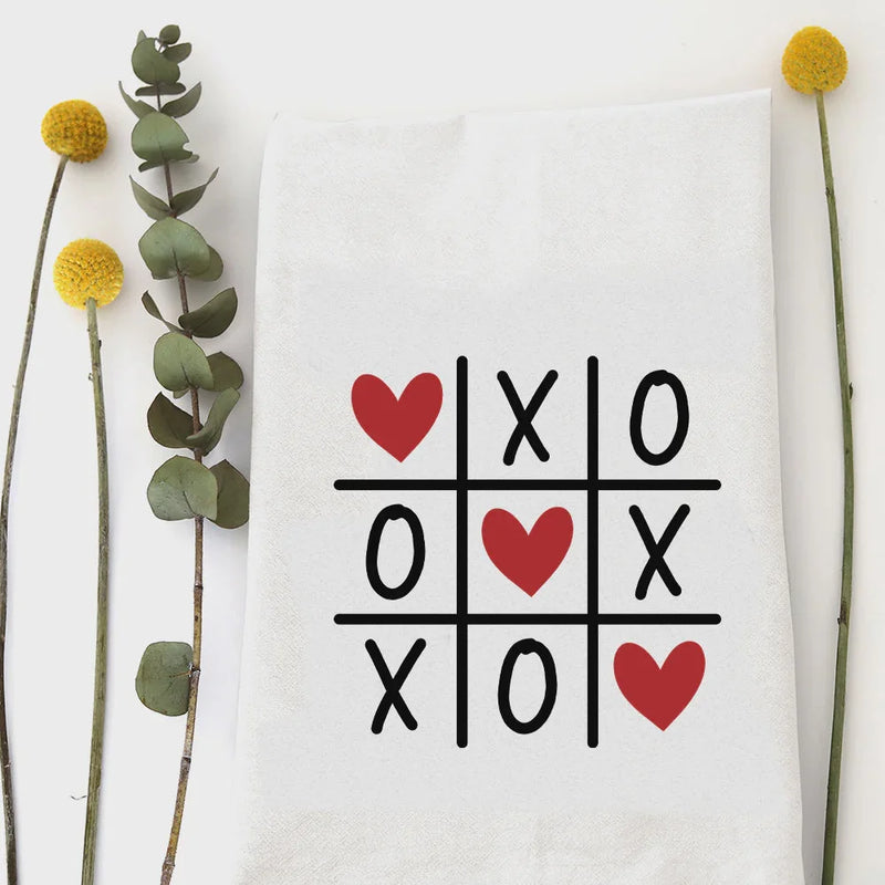 XOXO tea towel with white cotton tic-tac-toe design of red hearts and black Xs and Os