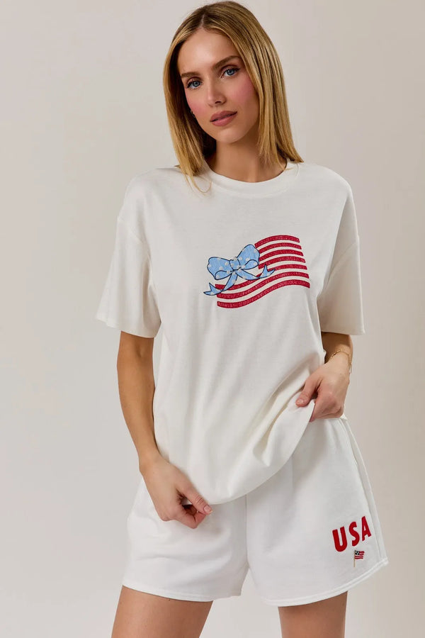 White cotton round neck t shirt with a glittery red and white usa flag graphic and blue bow design