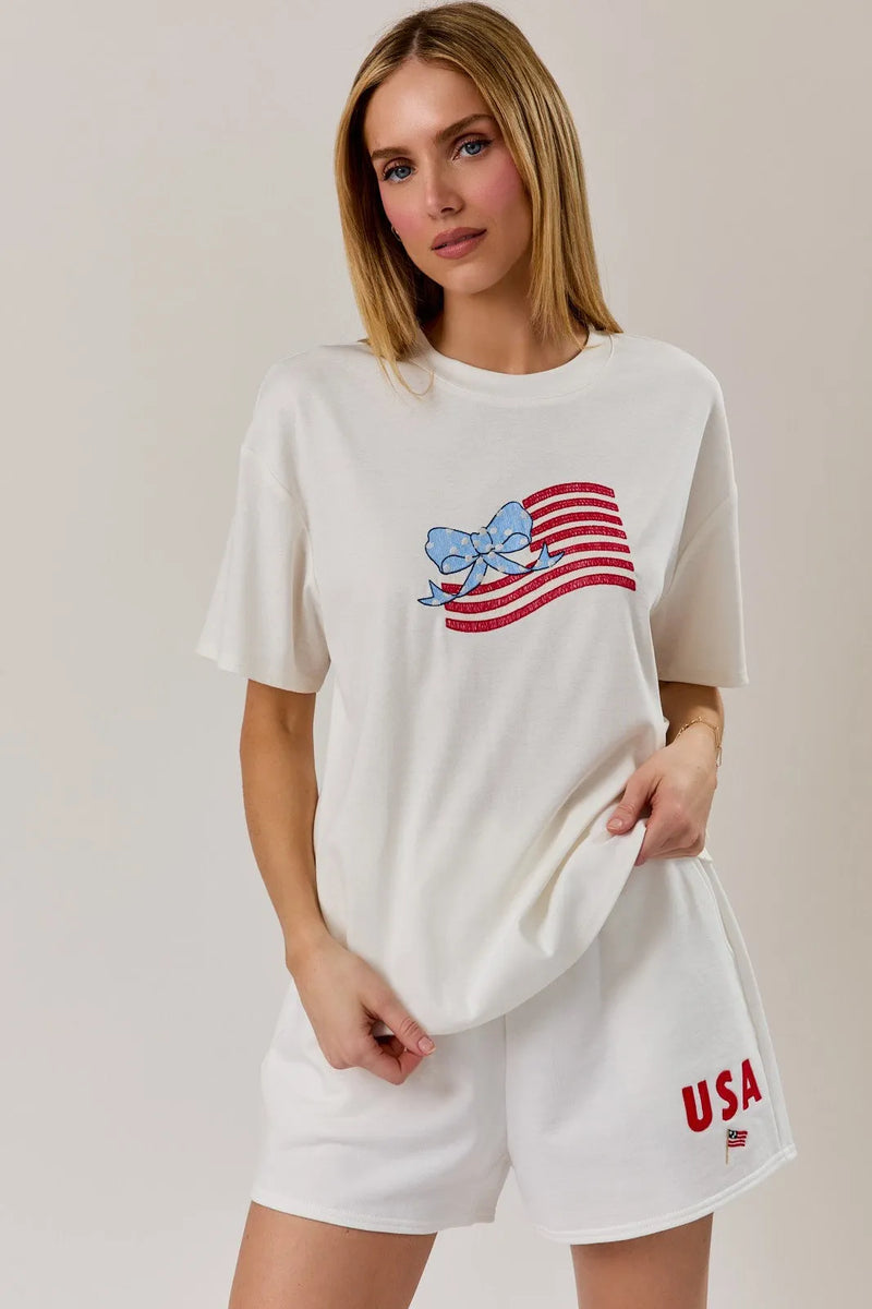 White cotton round neck t shirt with a glittery red and white usa flag graphic and blue bow design