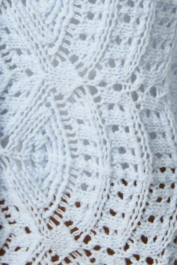 White crocheted lace fabric with intricate floral patterns on a long sleeve crochet light cardigan
